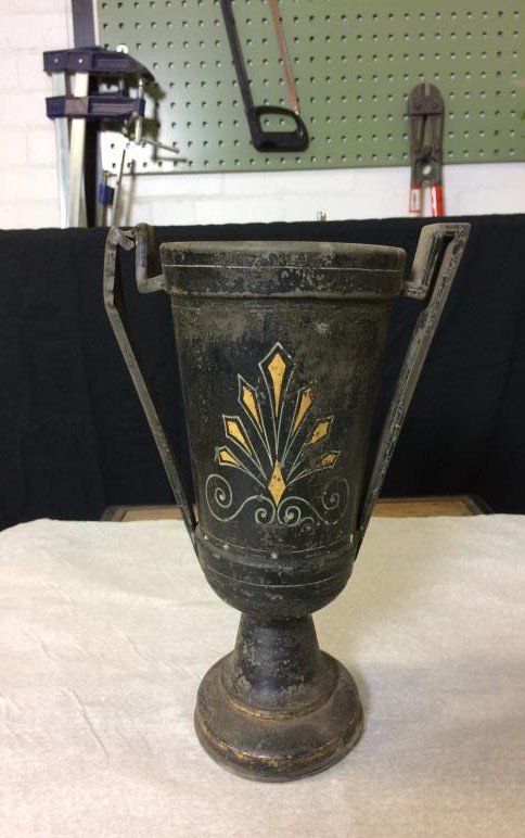 The metal vase from the stand, dirty, with a bent handle